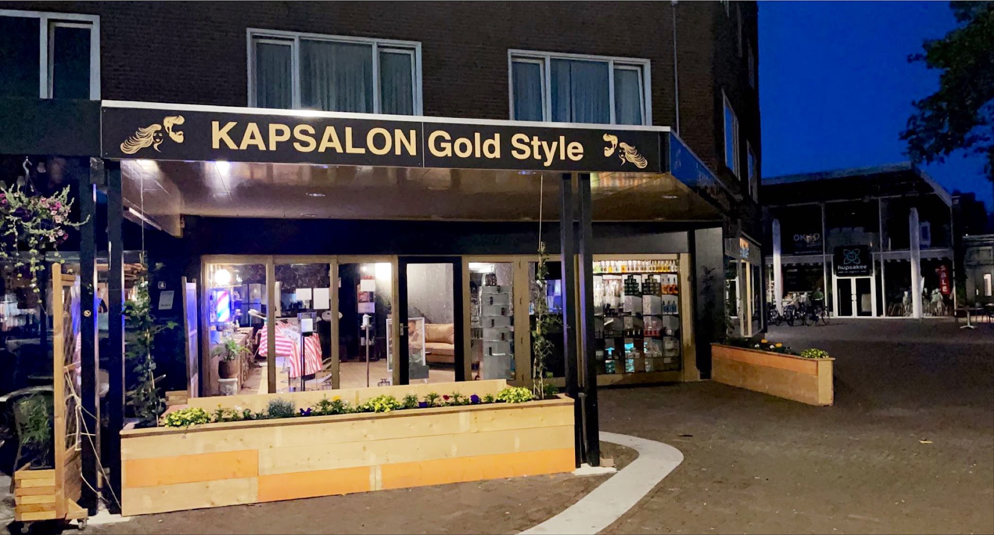 De gevel van Kapsalon Gold Style aan de Noorderstraat in Emmen in de avond, met het gouden uithangbord