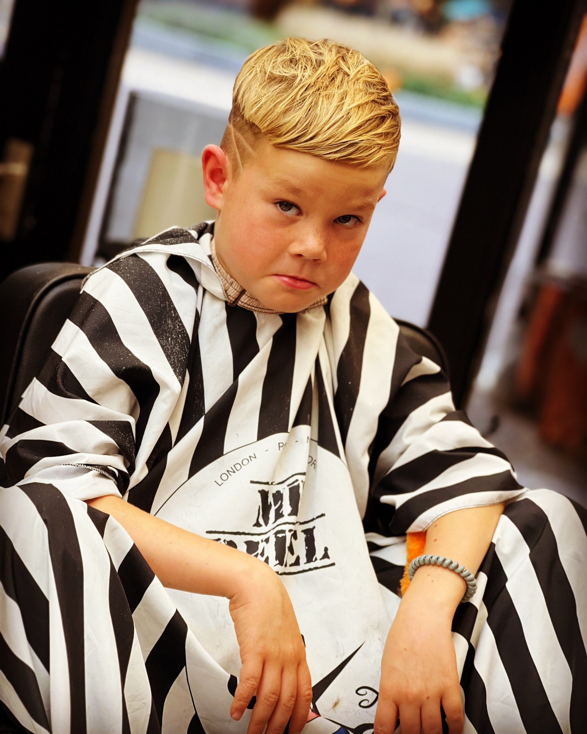 Jongen in gestreepte kapmantel met een fade en een lijn in het haar