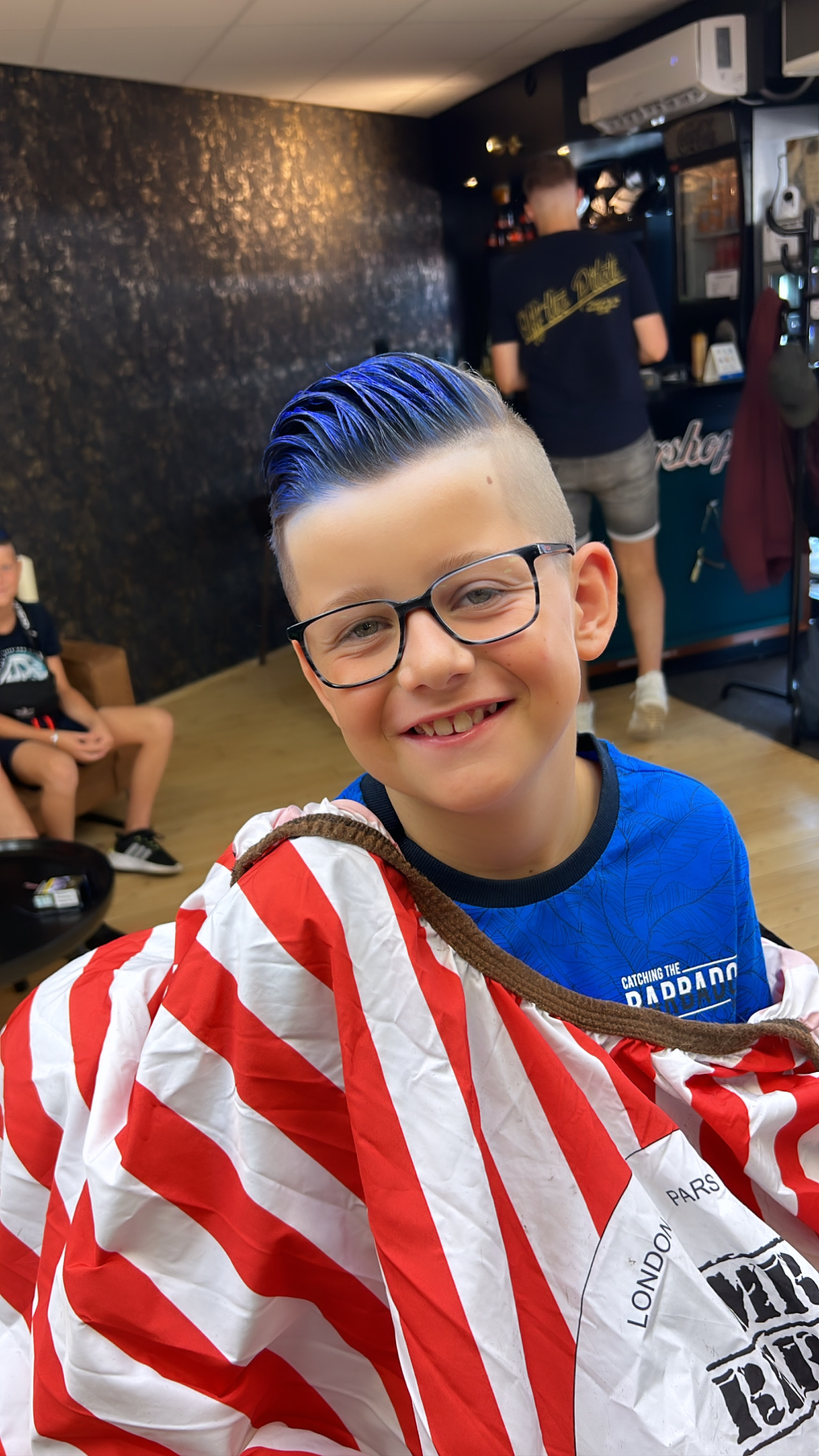 Lachende jongen met blauw gekleurd haar in de kappersstoel